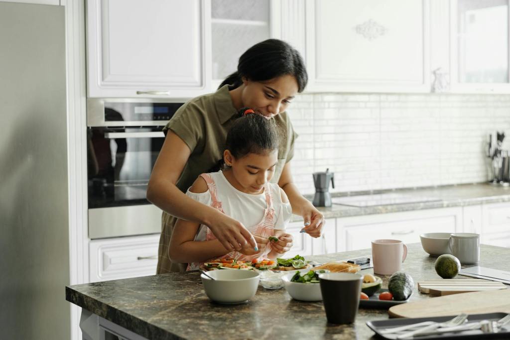 Mother helping her young daughter prepare a healthy meal in a bright kitchen, illustrating hands-on strategies from pediatric nutrition counseling to support picky eaters and build positive mealtime habits.